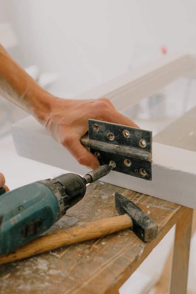 A handyman using a drill to install a hinge on a window frame indoors.